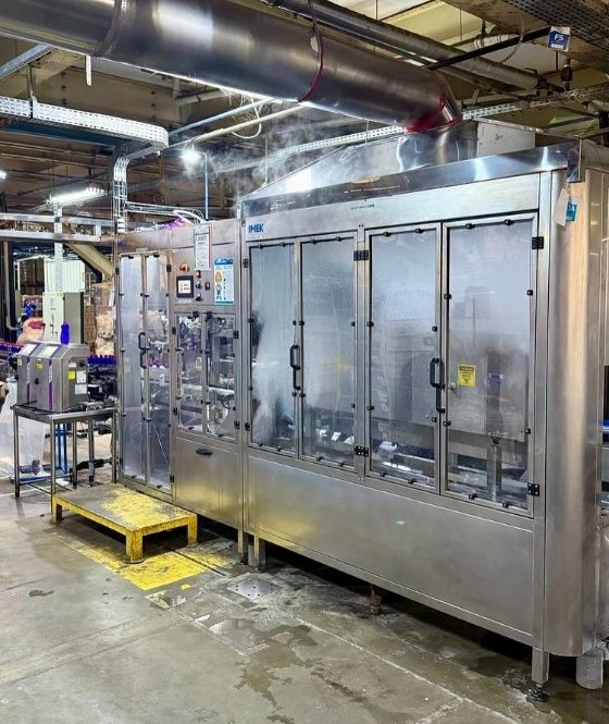 Rotuladora automática de sleeve IMEK aplicando rótulos termoencolhíveis em alta velocidade em linha de produção industrial moderna.